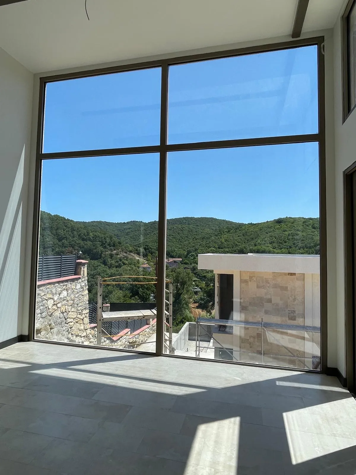 Salonun yüksek cam cephesi ve ormanlık tepeler
